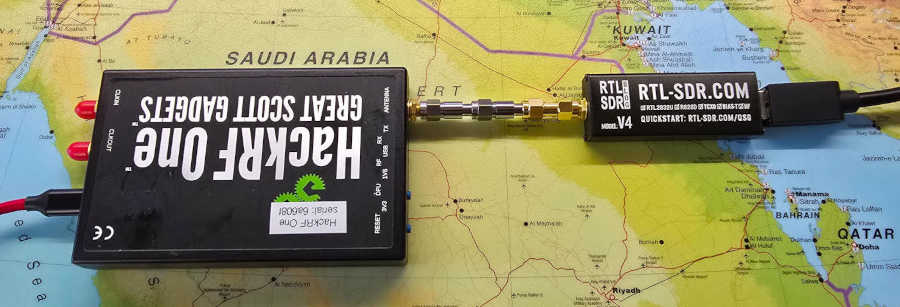 Overhead view of a HackRF on the left connected to a RTL-SDR on the right. The connection in between is a series of SMA attenuators and an adapter. USB cables connect the HackRF from the left and the RTL-SDR from the right.